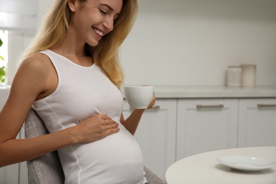 Photo of Beautiful pregnant woman drinking tea in kitchen