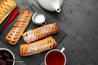 Photo of Fresh tasty puff pastry with sugar powder and tea served on grey table, flat lay. Space for text