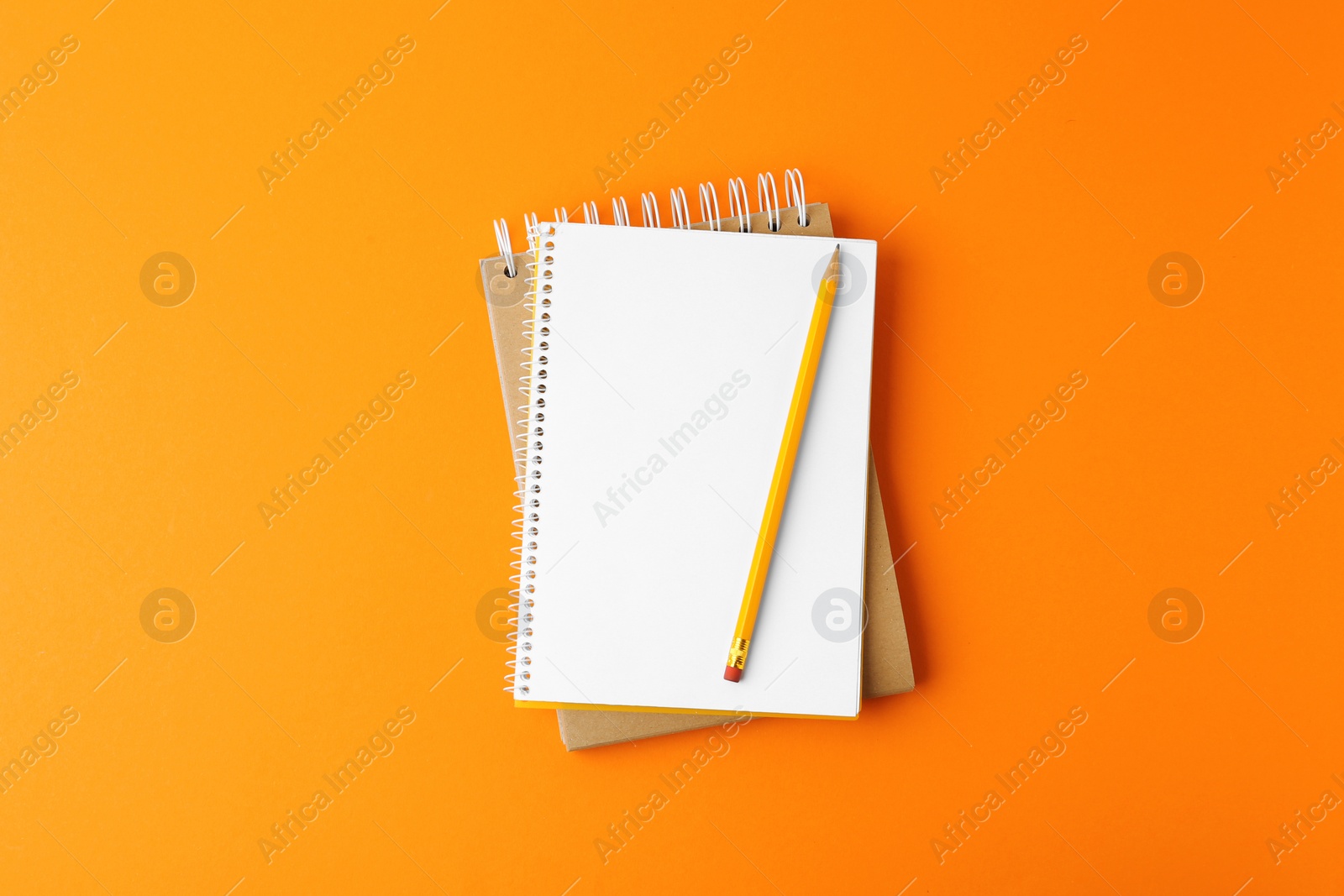 Photo of Notebooks with pencil on orange background, top view