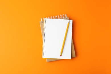 Notebooks with pencil on orange background, top view