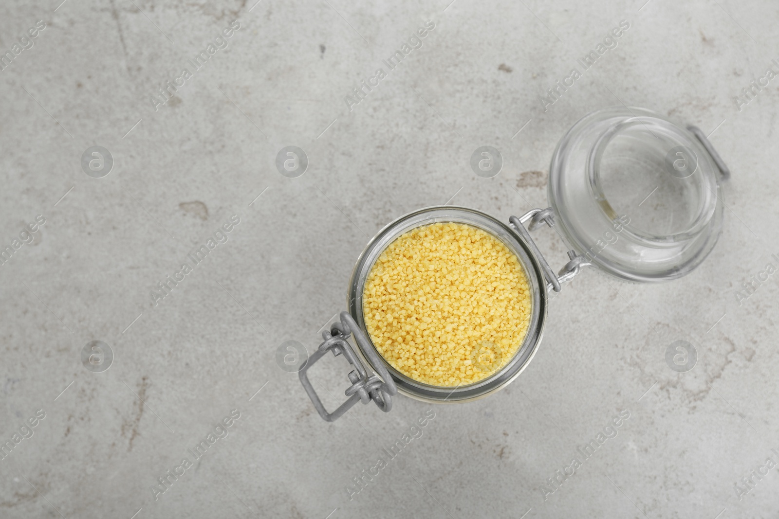 Photo of Glass jar of raw couscous on light table, top view. Space for text