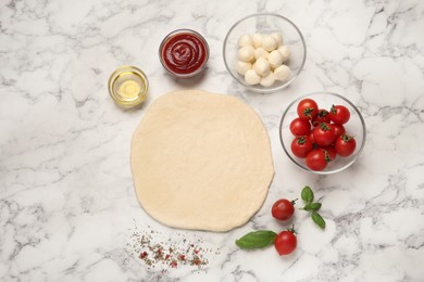 Photo of Raw pizza dough and other ingredients on white marble table, flat lay