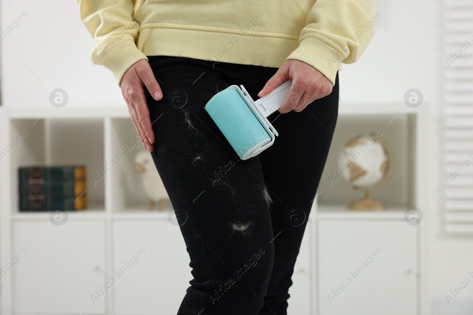 Photo of Woman with lint roller removing pet hair from black trousers indoors, closeup