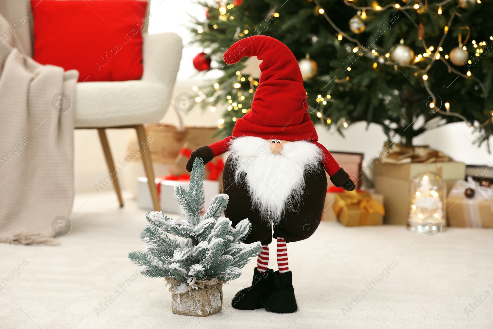 Photo of Funny Christmas gnome and tree on floor in room with festive decoration