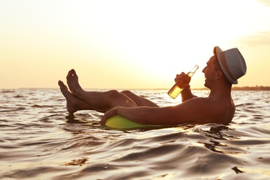 Photo of Young man with drink on inflatable ring in sea