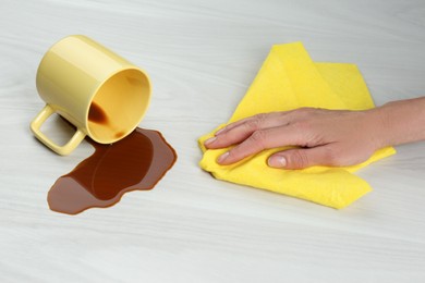 Photo of Woman cleaning spilled coffee on white wooden table, closeup