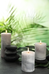 Photo of Burning candles and spa stones on grey table against blurred green background, space for text