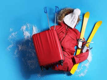 Suitcase with warm clothes and skis on light blue background, flat lay. Winter vacation