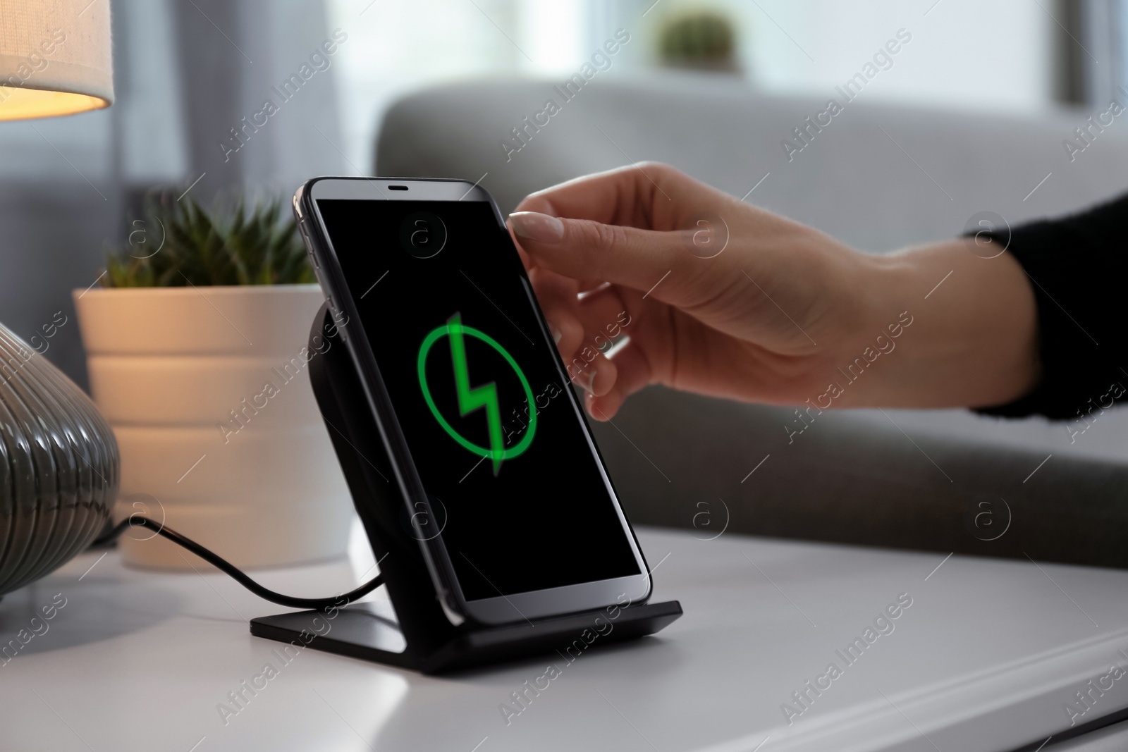 Photo of Woman taking smartphone from wireless charger in room, closeup