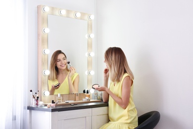 Photo of Woman applying makeup near mirror with light bulbs in dressing room