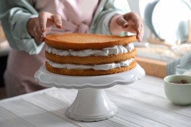 Woman stacking homemade sponge cakes at white wooden table, closeup