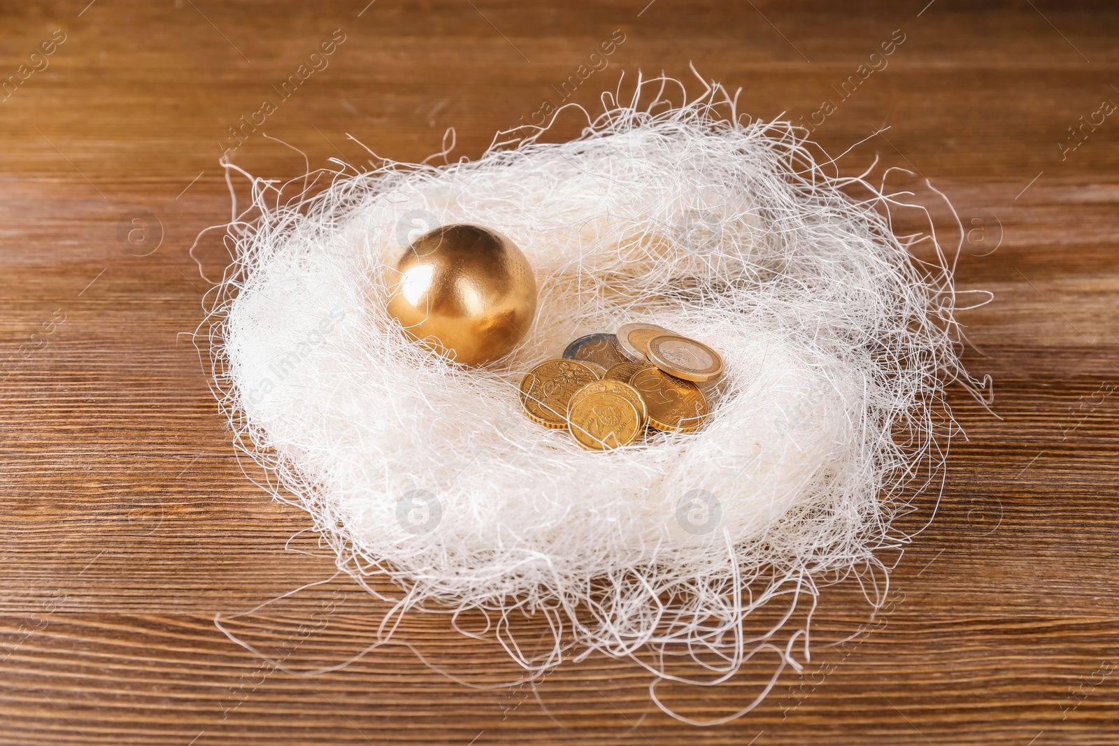 Photo of Golden egg and coins in nest on wooden table. Pension planning