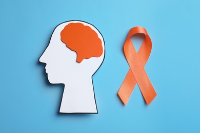 Photo of Human head cutout, brain and orange ribbon on light blue background, flat lay. Multiple sclerosis concept