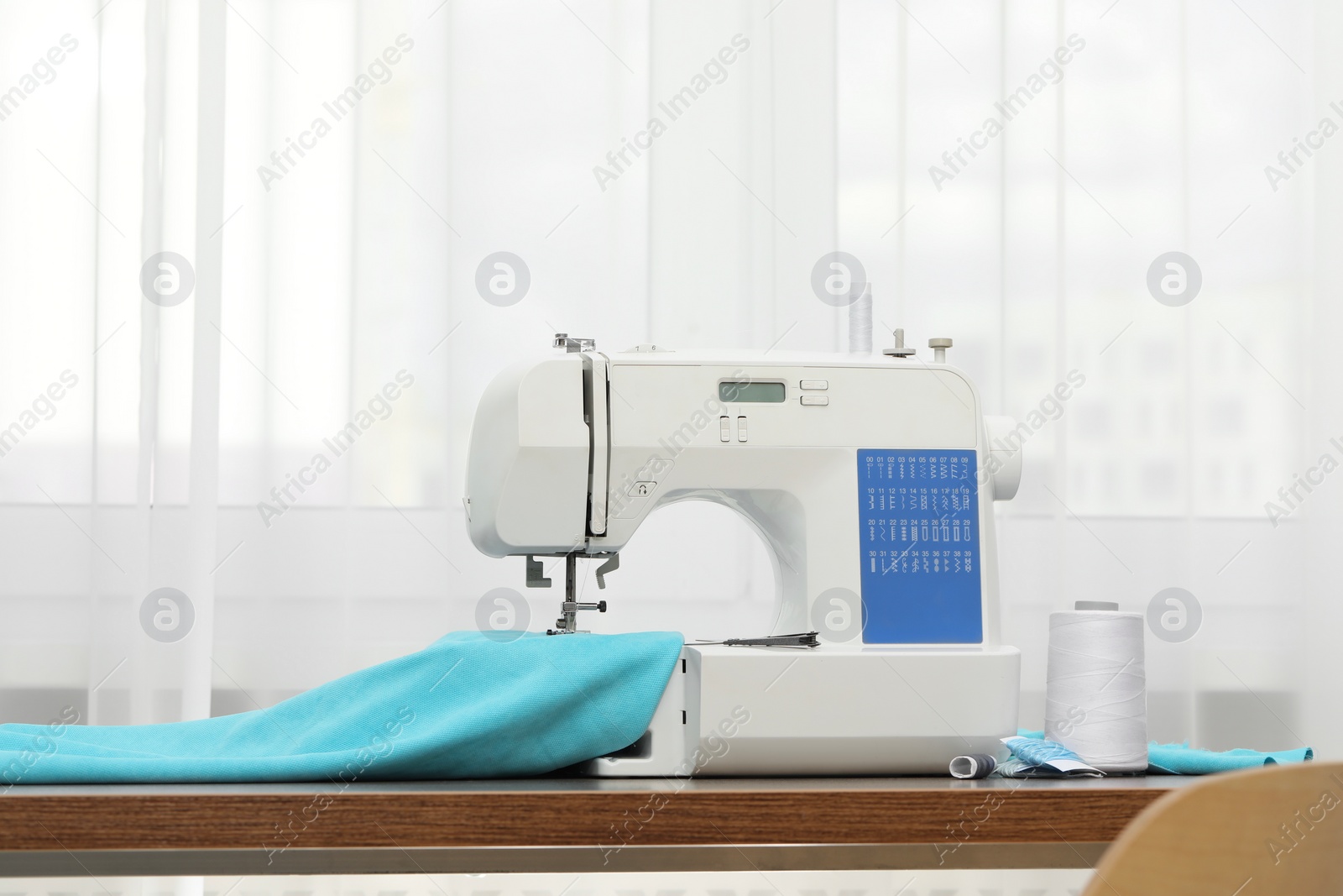 Photo of Sewing machine with fabric and craft accessories on wooden table indoors