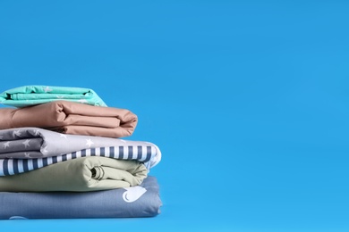 Photo of Stack of clean bed sheets on blue background. Space for text