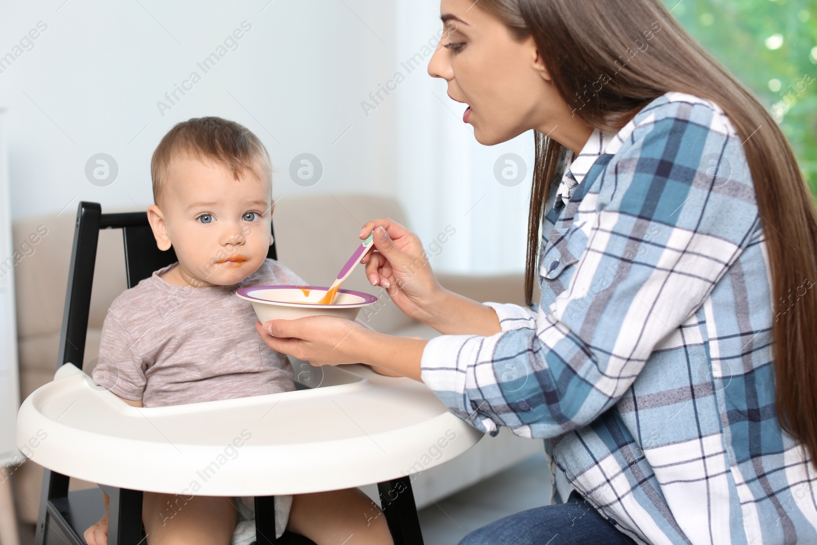 Photo of Woman feeding her child in highchair indoors. Healthy baby food