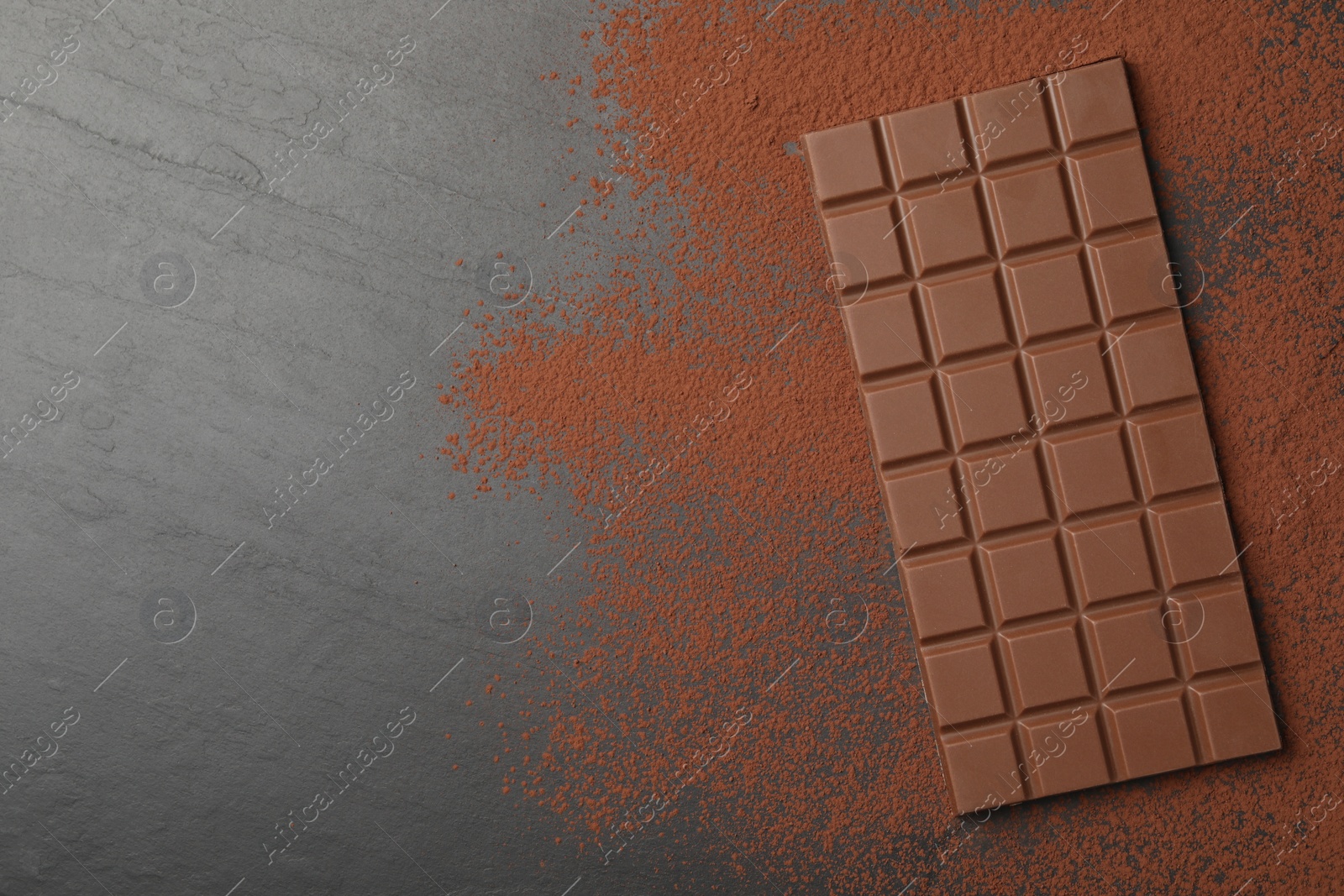 Photo of Tasty chocolate bar and cocoa powder on grey table, top view. Space for text