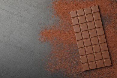 Photo of Tasty chocolate bar and cocoa powder on grey table, top view. Space for text