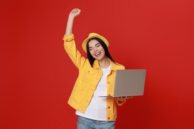 Emotional young woman with modern laptop on red background
