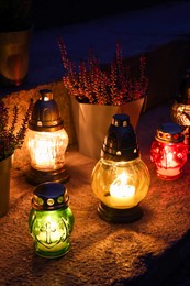 Different grave lanterns with burning candles on stone surface at night