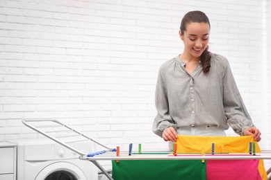 Photo of Young woman hanging clean laundry on drying rack indoors