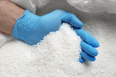 Person in gloves taking pellets of ammonium nitrate from bag, closeup. Mineral fertilizer