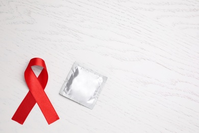 Red ribbon and condom on white wooden background, flat lay with space for text. AIDS disease awareness