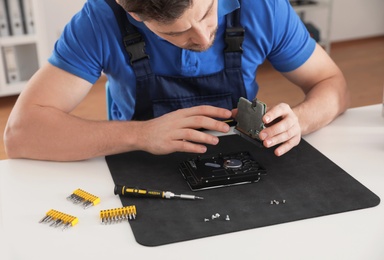 Male technician repairing hard drive at table indoors, closeup