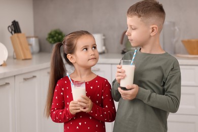 Cute children with glasses of fresh milk in kitchen