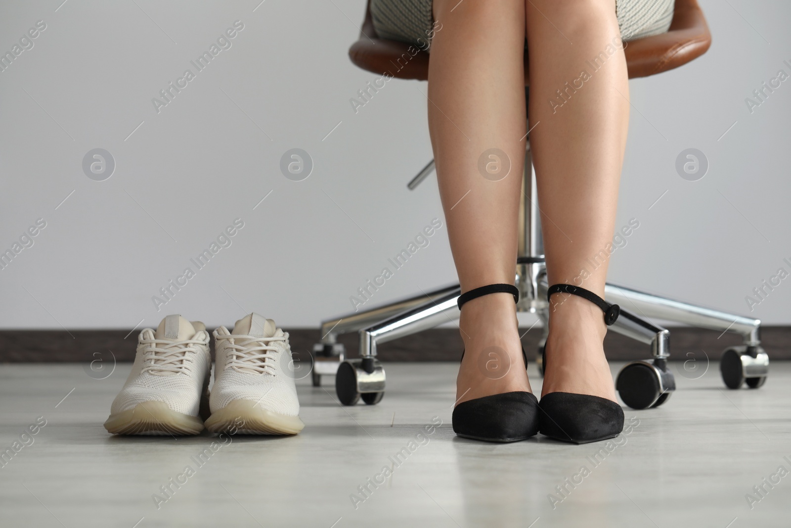 Photo of Comfortable sneakers near businesswoman wearing elegant shoes indoors, closeup