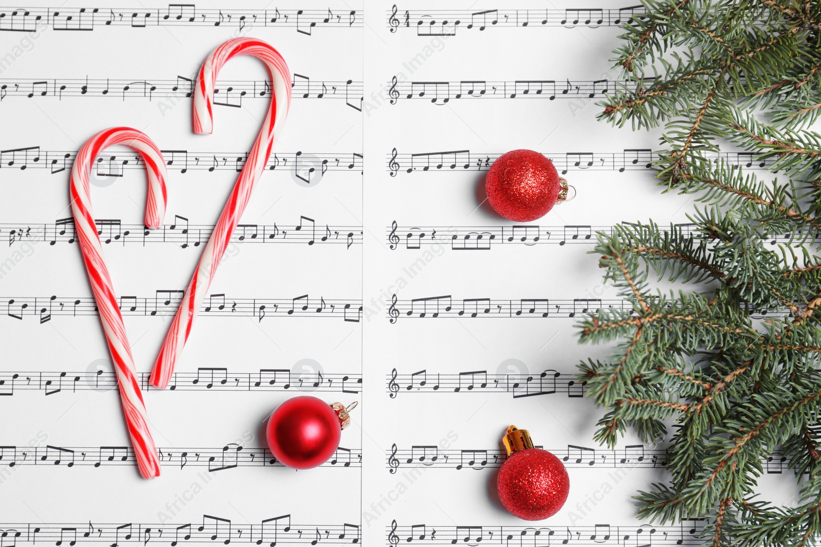 Photo of Composition with candy canes and Christmas balls on music sheets, top view