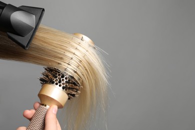 Photo of Hairdresser blow drying client's hair on light grey background, closeup. Space for text