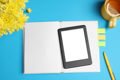 Photo of E-book reader with notebook, cup of tea and flowers on light blue background, flat lay. Space for text