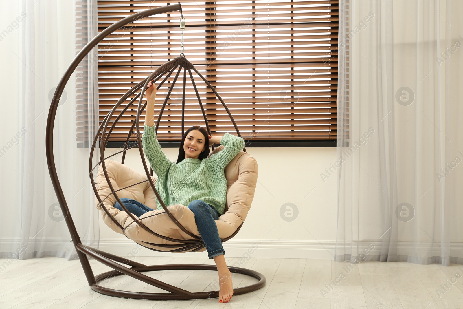 Photo of Young woman relaxing in hanging chair near window at home. Space for text