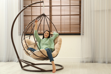 Photo of Young woman relaxing in hanging chair near window at home. Space for text