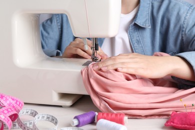 Photo of Seamstress working with sewing machine at white table indoors, closeup