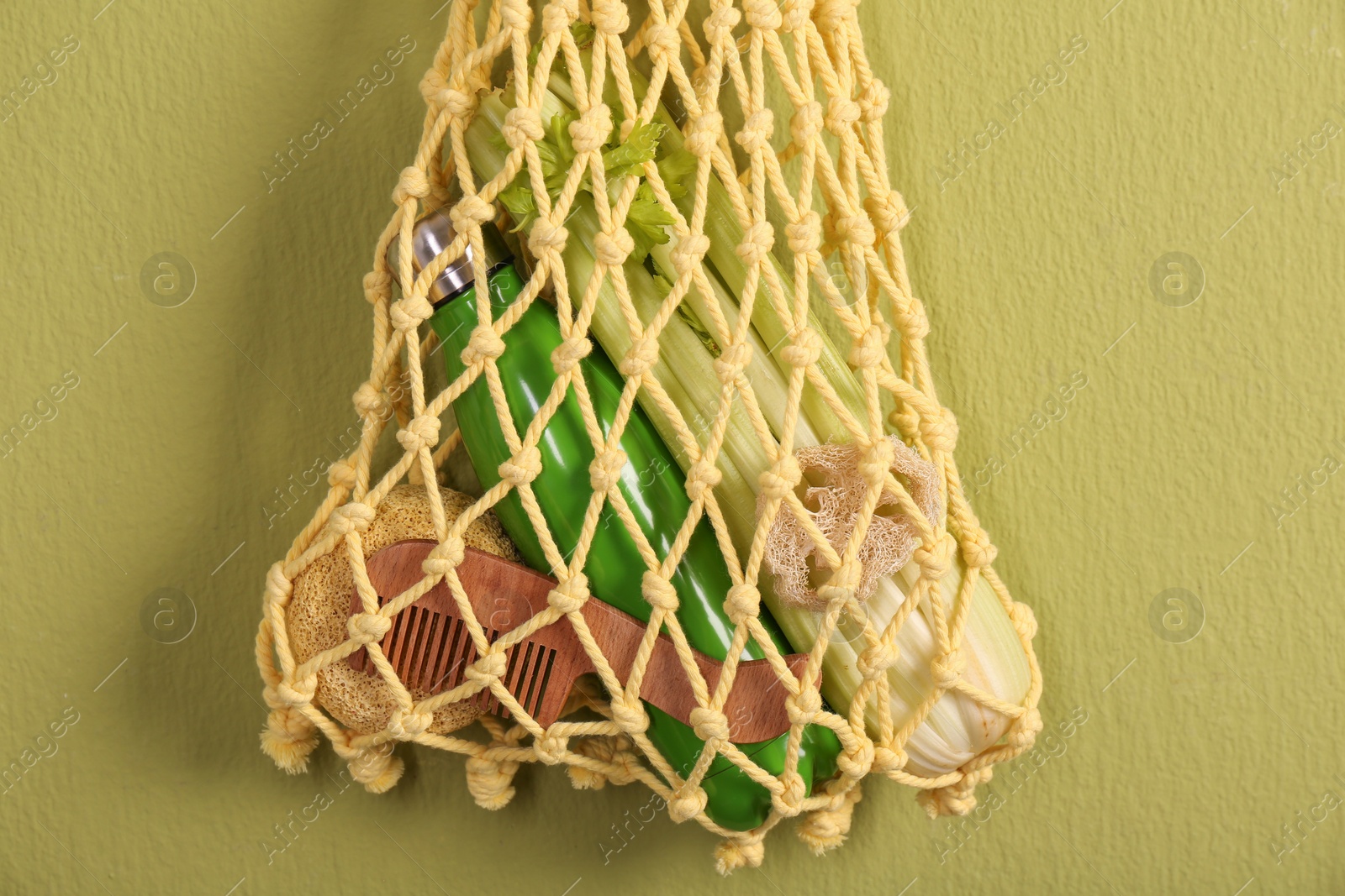 Photo of Conscious consumption. Net bag with eco friendly products hanging on olive wall, closeup