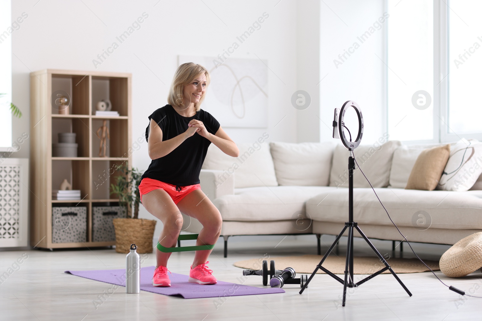 Photo of Smiling sports blogger streaming online fitness lesson with smartphone at home