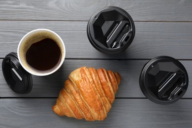 Photo of Coffee to go. Paper cups with tasty drink and croissant on grey wooden table, flat lay