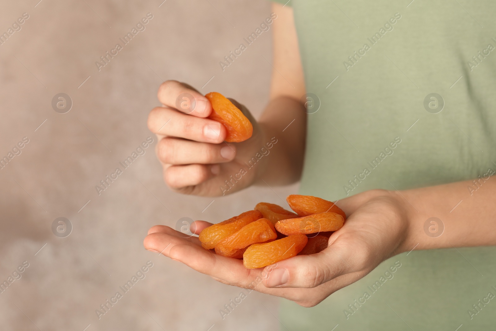 Photo of Woman holding handful of dried apricots on color background, space for text. Healthy fruit