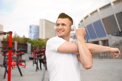 Photo of Man with headphones stretching before morning fitness near outdoor gym