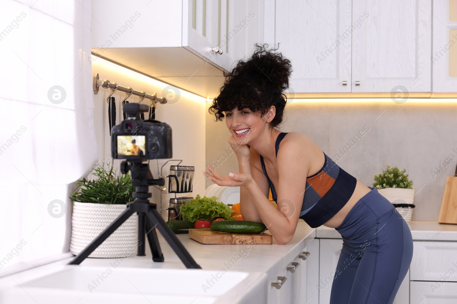 Photo of Smiling food blogger explaining something while recording video in kitchen