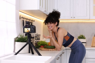 Photo of Smiling food blogger explaining something while recording video in kitchen