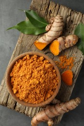 Photo of Aromatic turmeric powder and raw roots on grey table, top view