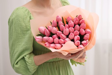 Photo of Woman holding bouquet of pink tulips indoors, closeup