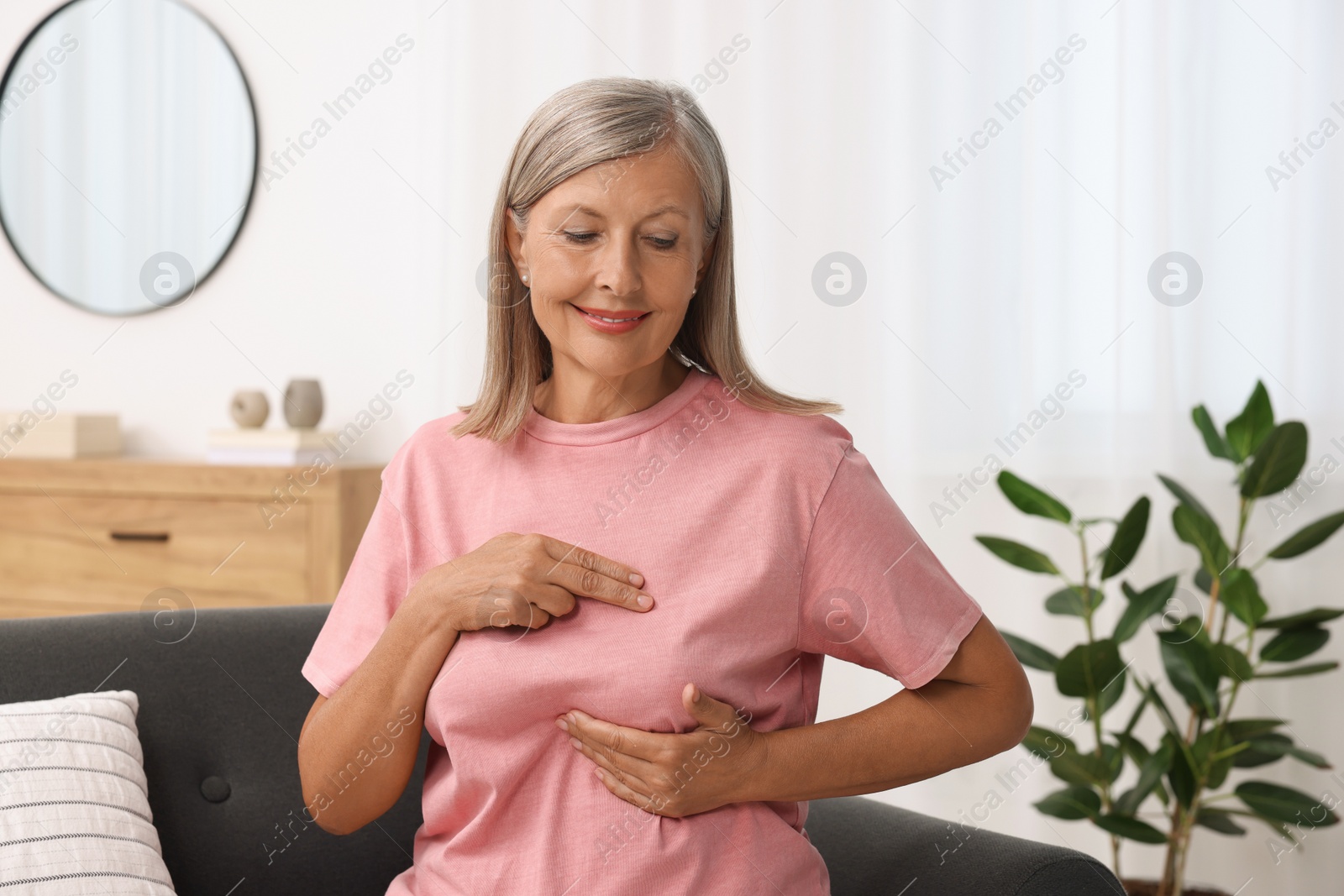 Photo of Beautiful senior woman doing breast self-examination at home