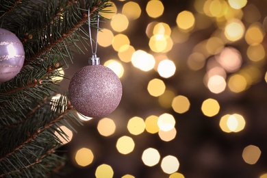 Shiny pink ball hanging on Christmas tree against festive lights. Space for text