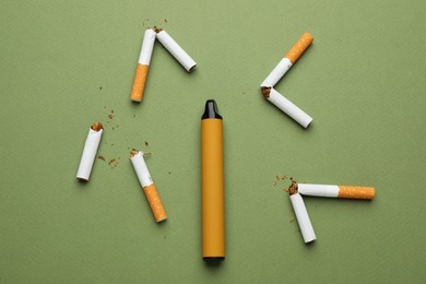 Photo of Disposable electronic smoking device surrounded by broken cigarettes on olive background, flat lay