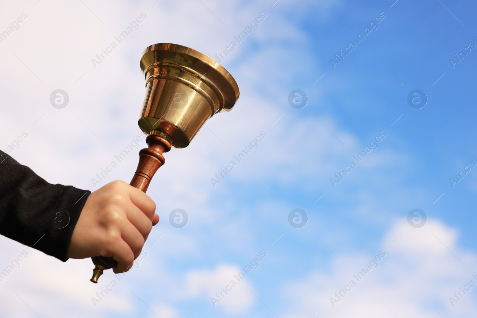 Photo of Pupil with school bell against cloudy sky, closeup. Space for text