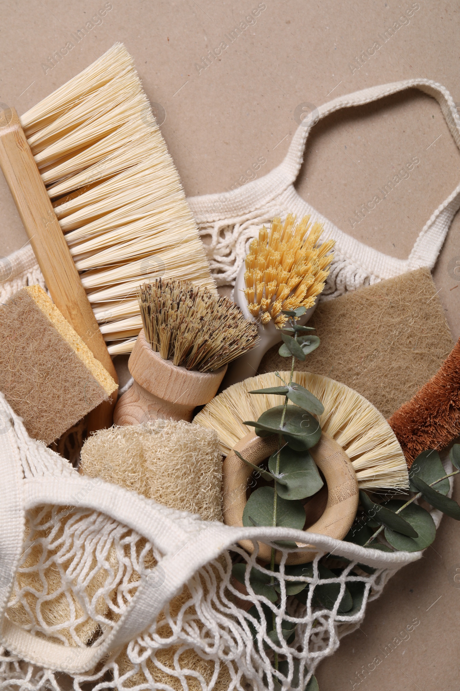 Photo of Cleaning brushes, sponges, eucalyptus leaves and string bag on pale brown background, top view